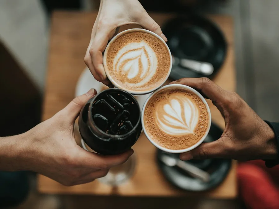 Three friends clinking coffee cups over a wooden table